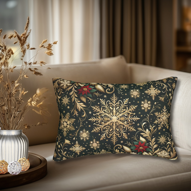 a decorative pillow with a black and gold floral pattern, placed on a white couch. The pillow has a red flower and snowflake design, adding a touch of color and elegance to the scene. The couch is positioned against a window, allowing natural light to illuminate the room. A vase with dried flowers and a tray with ornaments are also visible in the background, contributing to the cozy and festive atmosphere.